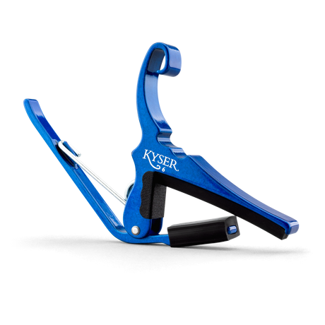 The image shows a bright blue Kyser guitar capo with a spring-loaded, curved clamp design. The "KYSER" name is visible on the metal body. It has black rubber padding to protect the guitar neck and strings while ensuring a secure grip. This quick-change capo is popular for easy one-handed use during performances, offering durability and an attractive anodized finish.