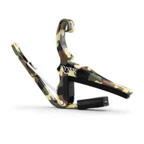 The image shows a KYSER spring-loaded guitar capo with a camouflage pattern in green, brown, and tan. It features a curved metal frame, a padded bar to press the strings, and a strap attachment point. This quick, one-handed capo evenly clamps all strings for clean sound and is popular among guitarists for easy use during performances.