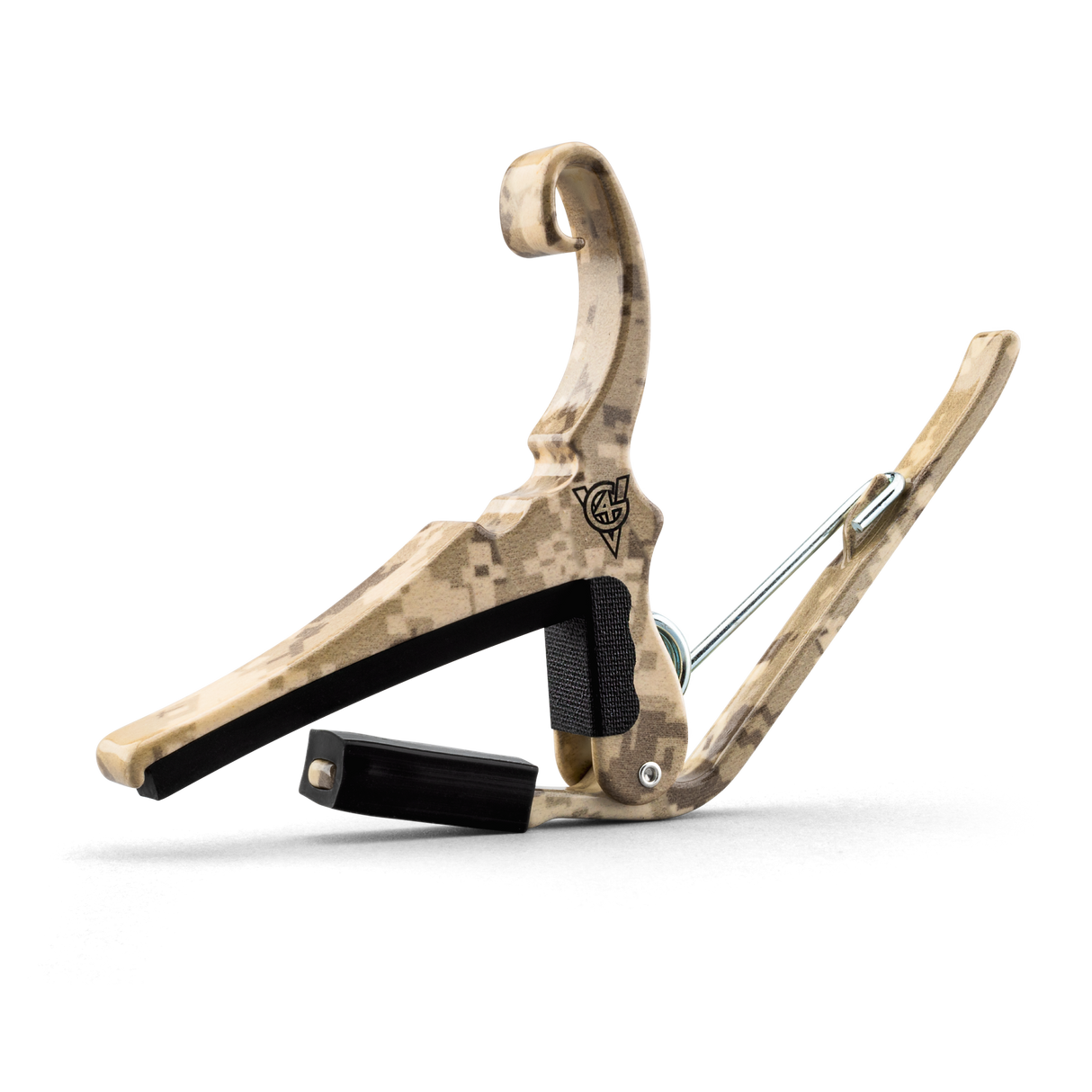 The image shows a guitar capo with a curved wooden frame featuring a tan and brown digital desert camouflage pattern. It has a black padded bar for pressing strings, a spring-loaded mechanism for easy attachment, metal hardware, and a visible logo on the frame. This capo allows guitarists to change string pitch by clamping the fretboard, offering a distinctive style compared to typical plain capos.