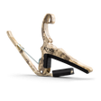 The image shows a Kyser Quick-Change guitar capo with a camouflage or wood-grain finish. It features a spring-loaded clamp with black padding to protect the fretboard and neck. The "KYSER" brand name is visible, and a black strap is attached for easy carrying. This popular accessory allows guitarists to quickly change pitch by clamping across the fretboard, enabling quick transposition with one-handed operation.