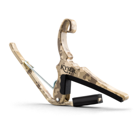 The image shows a Kyser Quick-Change guitar capo with a camouflage or wood-grain finish. It features a spring-loaded clamp with black padding to protect the fretboard and neck. The "KYSER" brand name is visible, and a black strap is attached for easy carrying. This popular accessory allows guitarists to quickly change pitch by clamping across the fretboard, enabling quick transposition with one-handed operation.
