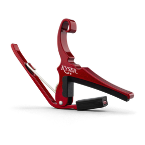 The image shows a Kyser spring-loaded, trigger-style guitar capo with a red anodized aluminum finish. It has black rubber padding to protect the guitar strings and neck while providing a secure grip. This popular accessory allows quick key changes by clamping all strings at any fret. Its curved design fits the guitar neck for even pressure, and the spring mechanism enables easy one-handed use.