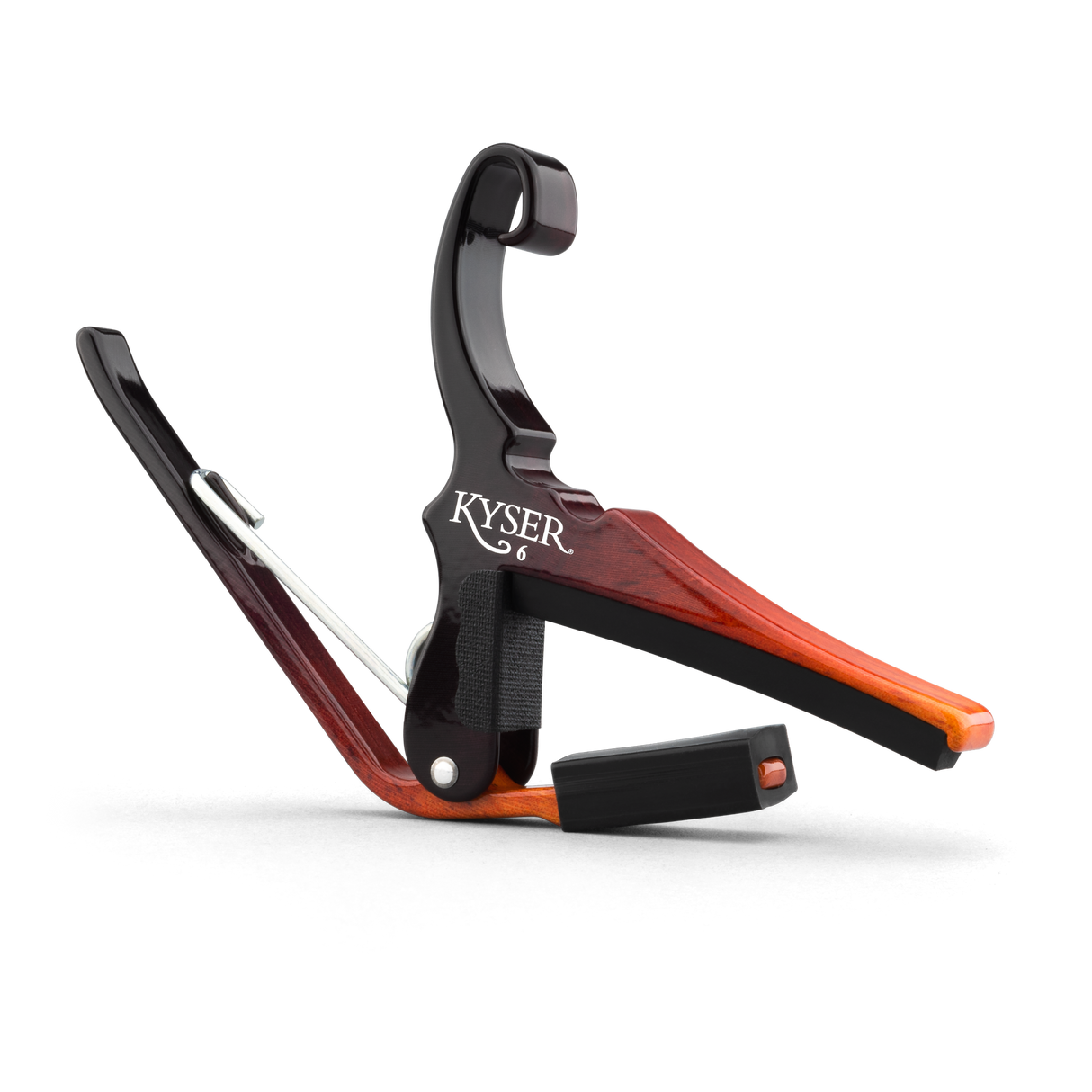 The image shows a Kyser guitar capo with a wood-grain finish in reddish-brown tones. This spring-loaded clamp attaches to the fretboard, raising the pitch of all strings for easy key changes without new chords. It features padded surfaces to protect the guitar and a quick-release handle for fast adjustments. Kyser capos are trusted by acoustic and electric guitarists for reliability and ease of use.