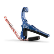 The image shows a Kyser spring-loaded guitar capo with a patriotic American flag design, featuring blue with white stars and red and white stripes. This essential accessory clamps the fretboard to raise string pitch, allowing easy key changes. Kyser capos are popular among guitarists for their functionality and quick one-handed use, combining practicality with a distinctive, decorative look.