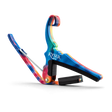 The image shows a colorful Kyser guitar capo with a vibrant tie-dye pattern featuring blues, reds, and oranges. It is spring-loaded with a curved clamp and has black padding to protect the guitar neck and strings. A small black cylindrical pick holder is integrated into the design. This accessory clamps the fretboard to change string pitch, combining functionality with a bright, artistic look.