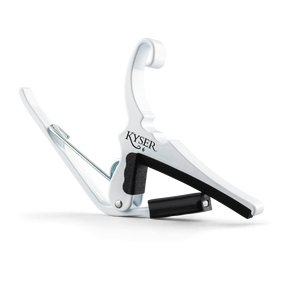 The image shows a white Kyser Quick-Change Capo, a spring-loaded clamp for guitar fretboards. It features a curved design with black rubber padding to protect the neck and frets. The capo allows easy one-handed use, enabling guitarists to change keys quickly while playing. Kyser is a popular brand known for its reliable, fast placement capo models favored by many guitarists.