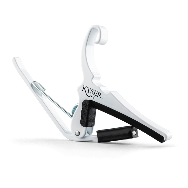 The image shows a white Kyser Quick-Change Capo, a spring-loaded clamp for guitar fretboards. It features a curved design with black rubber padding to protect the neck and frets. The capo allows easy one-handed use, enabling guitarists to change keys quickly while playing. Kyser is a popular brand known for its reliable, fast placement capo models favored by many guitarists.