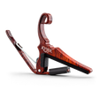 The image shows a KYSER spring-loaded guitar capo with a reddish-brown wood grain finish. It features a curved clamp arm, a padded black bar to protect strings, and a quick-release handle for easy one-handed use. Designed to clamp the fretboard and raise string pitch, this elegant capo is a practical and stylish accessory that helps guitarists change keys and achieve different chord voicings effortlessly.