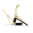 The image shows a Kyser Quick-Change guitar capo with a cream-colored metal body. It features a spring-loaded, lever-style mechanism for easy one-handed use, black rubber padding to protect the guitar, and a curved design to fit the neck. This accessory clamps across the fretboard to raise pitch, enabling guitarists to play in different keys while using familiar chord shapes.