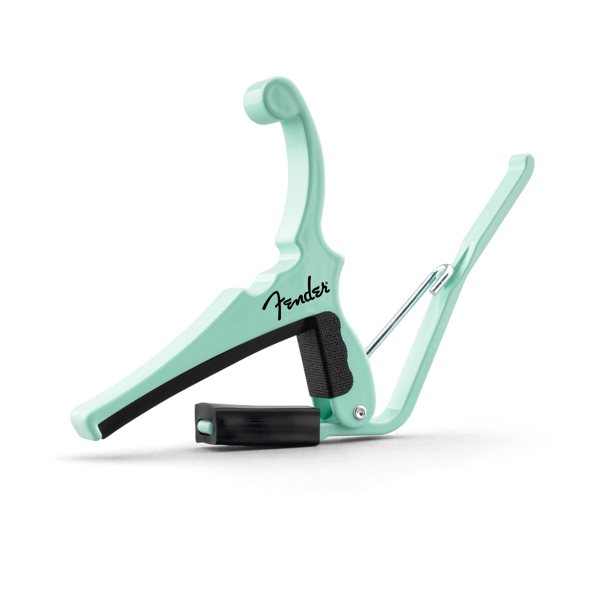 The image shows a mint green Fender guitar capo with the black Fender logo in script. It features a spring-loaded mechanism, a black rubber-padded clamp to press the strings, and a curved arm to open and position it on the guitar neck. This accessory changes string pitch by shortening their length, enabling different keys with the same chord shapes. Its clean design combines functionality and style.