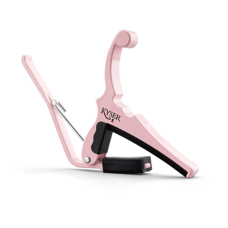 The image shows a pink Kyser guitar capo with a spring-loaded, curved handle for one-handed use. It features black rubber padding to protect the guitar neck, the "KYSER" logo on the clamp, and a sleek, ergonomic design typical of Kyser’s Quick-Change series. This capo, suitable for acoustic and electric guitars, allows players to change pitch easily while adding a stylish, personalized touch.