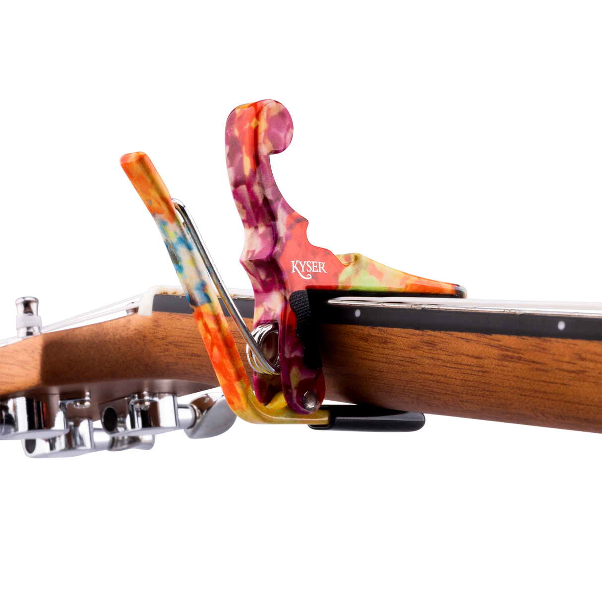 The image shows a Kyser guitar capo with a vibrant, swirled design in orange, purple, pink, and other colors, attached to the neck of an acoustic guitar. The capo features a spring-loaded mechanism for quick, one-handed use. Its colorful, tie-dye style finish adds a decorative touch to this essential accessory that clamps the fretboard to raise the pitch and enable easy key changes while maintaining chord fingerings.