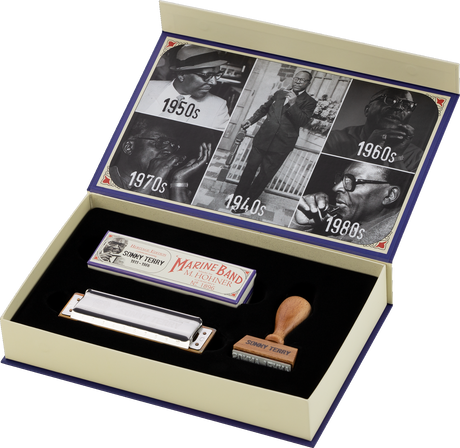 The image shows a commemorative set featuring a Hohner Marine Band harmonica, its original packaging, and a wooden stamp engraved with "SONNY TERRY." The elegant box lid displays vintage black-and-white photos from the 1940s to 1980s, documenting the history of blues music. This special edition honors blues harmonica legend Sonny Terry, combining a classic instrument with historical imagery for collectors.