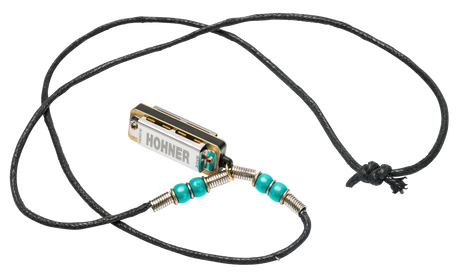 The image shows a small Hohner harmonica creatively repurposed as a wearable necklace. It features a chrome and gold body with the Hohner logo, attached to a black braided cord with turquoise beads and metal wire wraps. The necklace includes an adjustable sliding knot closure. This unique design blends functionality and fashion, allowing musicians to carry and potentially play their instrument as wearable art.