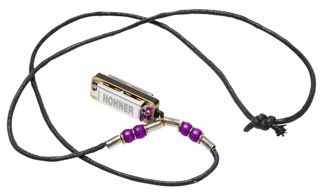 The image shows a Hohner harmonica transformed into a wearable necklace. The small, chrome harmonica with gold trim features the Hohner logo and is suspended on a black braided cord. Purple beads flank the instrument, connected by metal coils, creating a handcrafted, artistic look. This unique accessory allows musicians to keep their harmonica handy while making a stylish statement.