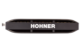 The image shows a Hohner harmonica, a well-known brand in the harmonica industry. It features a classic 10-hole diatonic design with a black comb and brass reed plates visible on top and bottom. The brand name "HOHNER" is prominently displayed in white on the body. Hohner, a German company since 1857, produces harmonicas used in many musical genres like blues, folk, and rock.