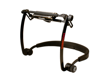 The image shows a Hohner harmonica holder with a black metal frame and adjustable padded neck strap for hands-free play. The holder secures the harmonica, displays the "HOHNER" brand, and allows tilting for customized positioning. Commonly used by folk and blues musicians, it enables playing harmonica while playing other instruments. The sturdy, professional design suits practice and live performance.