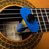 The image shows a classical acoustic guitar with a natural wood finish and a decorative rosette around the sound hole. A blue cylindrical guitar humidifier is inserted in the sound hole to protect the wood. Nylon strings are visible, and sheet music or tablature can be seen through the sound hole, indicating active use and proper maintenance of the instrument.