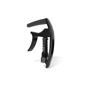 The image shows a black, spring-loaded clamp-style guitar capo with a curved mechanism, padded bar, and ergonomic handle for one-handed use. Made from metal and rubber or silicone, it features a sleek, modern design. This accessory clamps across the fretboard to raise string pitch, allowing guitarists to change keys easily while maintaining chord shapes. It appears to be a high-quality, professional-grade model.