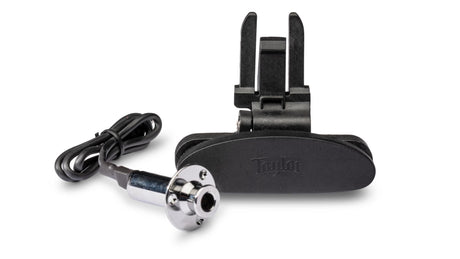 The image shows a Taylor acoustic guitar pickup and preamp system, featuring a black pickup unit, a branded control/preamp module with prongs, and a cable with a chrome 1/4" jack connector. This professional-grade system captures the guitar’s sound and allows amplification while preserving natural tone, commonly used by musicians for high-quality acoustic instrument amplification.