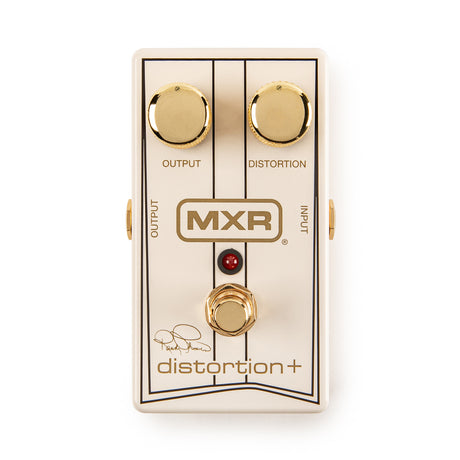 The image shows an MXR Distortion+ guitar effects pedal with a white/cream housing, gold accents, and two gold knobs labeled "OUTPUT" and "DISTORTION." It features a red LED indicator, a gold footswitch, the MXR logo in the center, the model name at the bottom, and a signature, likely from a notable guitarist. This classic pedal is known for its warm, tube-like distortion favored in rock, metal, and blues music.