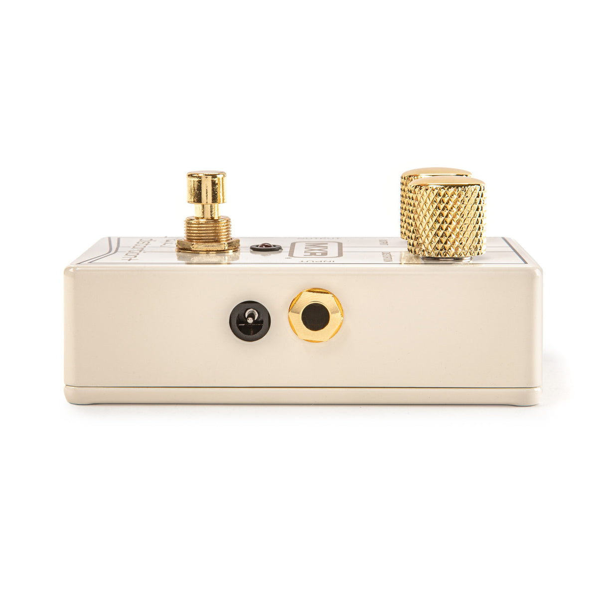 The image shows a cream-colored guitar effects pedal with gold hardware. The top panel features a gold threaded input jack on the left, a large gold knurled knob on the right, and a small switch or control markings in the center. The side panel has two jacks, one black and one gold. The pedal is compact and sturdy, designed to shape guitar tones for both studio and live use.