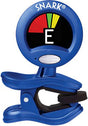 The image shows a Snark clip-on guitar tuner with a blue plastic body and spring-loaded clip. It features a circular screen displaying a chromatic tuner interface with a needle moving between red and green zones to indicate tuning. The letter "E" is shown, and a colorful arc provides visual tuning feedback. This compact, battery-powered device senses string vibrations, allowing tuning in noisy environments for guitars and other stringed instruments.