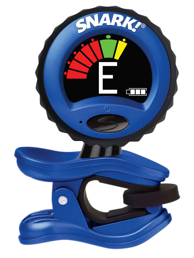 The image shows a Snark clip-on electronic tuner with a blue and black design and the "SNARK!" logo at the top. Its circular LCD displays the note "E" with a color-coded meter (red, green, yellow) indicating tuning status, plus a battery indicator. The tuner clips onto instrument headstocks and has a power button. It detects vibrations for accurate tuning, ideal for noisy environments.