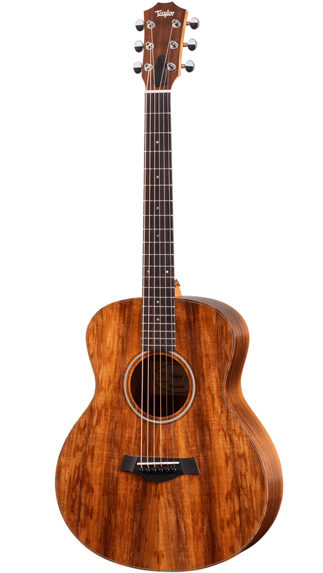 The image shows a beautiful Taylor steel-string acoustic guitar with a medium-sized Grand Auditorium body. It features a rich koa or mahogany wood grain with amber tones, chrome tuning machines, a dark wood bridge with a compensated saddle, a traditional round soundhole with a decorative rosette, and a dark ebony or rosewood fretboard with dot markers. This high-quality instrument is suited for recording, performing, or serious playing.