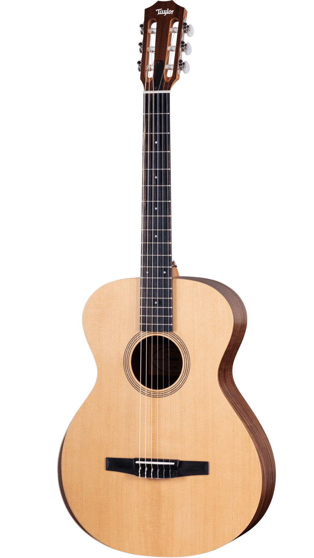 The image shows a Taylor classical guitar with a natural wood top and darker back and sides. It features a wide neck with a dark fretboard, six nylon strings, a slotted headstock with chrome tuners, and a black tie-block bridge. The round sound hole has a decorative rosette. This nylon-string acoustic guitar likely belongs to Taylor’s classical line, showcasing traditional design and craftsmanship.