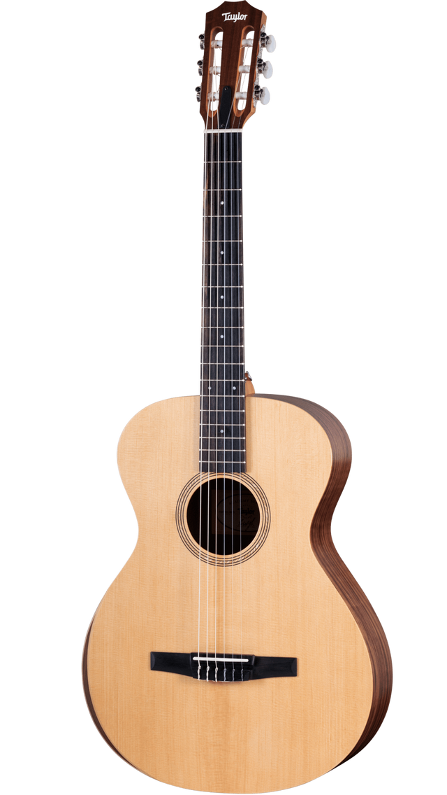 The image shows a Taylor classical guitar with a natural wood top and darker back and sides. It features a wide neck with a dark fretboard, six nylon strings, a slotted headstock with chrome tuners, and a black tie-block bridge. The round sound hole has a decorative rosette. This nylon-string acoustic guitar likely belongs to Taylor’s classical line, showcasing traditional design and craftsmanship.