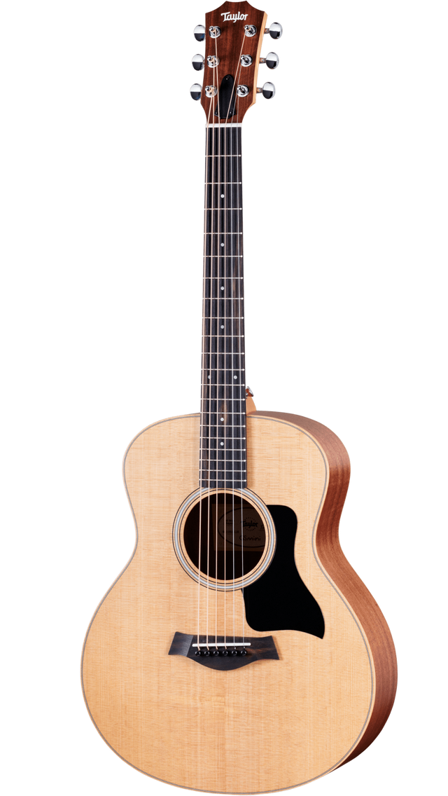 The image shows a Taylor steel-string acoustic guitar with a natural spruce or cedar top and darker mahogany or sapele back and sides. It features a mid-sized Grand Auditorium body, chrome tuning machines, a dark wood bridge with a compensated saddle, a round soundhole with a rosette, and a black pickguard. The natural finish highlights the wood grain, reflecting Taylor’s quality craftsmanship and versatile playability.