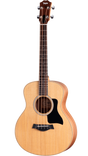 The image shows a Taylor 4-string acoustic bass guitar with a natural wood finish. It features a dark wood headstock with the Taylor logo and chrome tuners, a dark fingerboard with dot markers, a round sound hole with a decorative rosette, a black pickguard, and a dark wood bridge likely with an integrated pickup. This high-quality instrument is known for its warm, mellow tone ideal for unplugged and recording use.