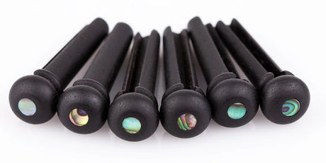 The image shows a collection of dark acoustic guitar bridge pins with decorative iridescent inlays resembling abalone or mother-of-pearl. These cylindrical pins secure the strings at the guitar bridge, enhancing both the instrument’s appearance and functionality. The colorful inlays help identify different strings and provide a stylish upgrade to standard bridge pins.