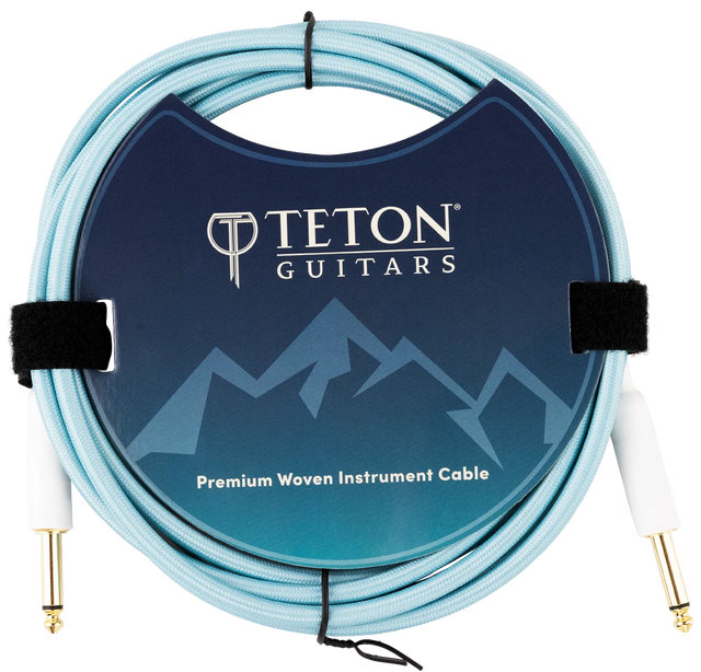 The image shows a Teton Guitars Premium Woven Instrument Cable with a light blue/turquoise woven fabric exterior for durability and style. It has gold-plated 1/4" connectors on both ends for optimal signal transfer. The packaging features the Teton Guitars logo and mountain design. The cable is coiled and secured with velcro straps, highlighting its quality build ideal for electric guitars and basses.