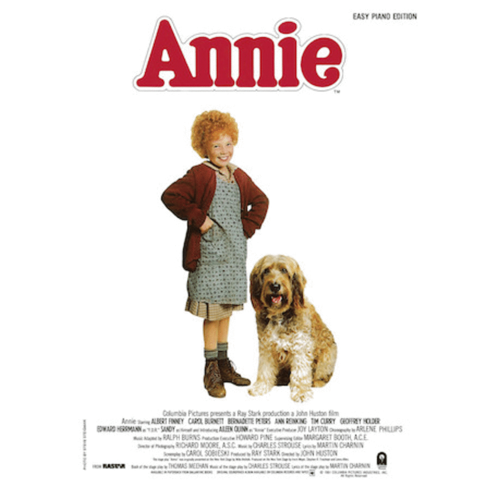 The image shows the cover of an easy piano edition songbook for the musical "Annie." It features the red "Annie" logo at the top, with a young girl with curly red hair standing next to a large shaggy dog, representing the characters Annie and Sandy. This sheet music includes simplified piano arrangements of popular songs from the Broadway show.