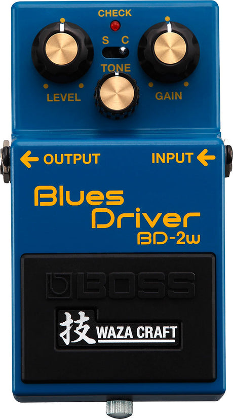The image shows a Boss Blues Driver BD-2W guitar effects pedal, Waza Craft edition. It features LEVEL, TONE, and GAIN knobs, a CHECK light, and an S/C switch for Standard or Custom voicings. The blue compact pedal has INPUT/OUTPUT jacks, Boss branding, and Japanese "Waza" characters. The BD-2W offers classic and custom overdrive modes, delivering smooth, bluesy distortion favored across many music genres.