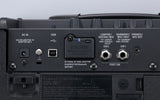 The image shows the back panel of a Roland CUBE-ST2 guitar/bass amplifier featuring a DC IN jack, USB port, various input/output jacks (LOOPER/GUITAR/MIC, HARMONY/MIC/INST, PHONES/REC OUT), SW1 and SW2 function switches, FOOT SW connection, a slot for BOSS Bluetooth Audio MIDI Dual Adaptor, battery compartment for AA batteries, and compliance labels. It highlights the amp's blend of analog and digital features, including built-in effects and wireless connectivity.