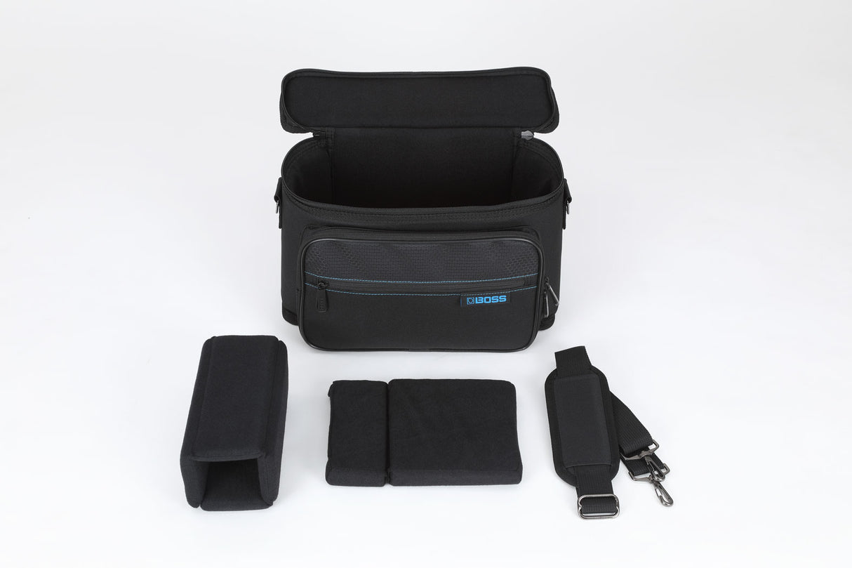 The image shows a black BOSS-branded gig bag with blue stitching, opened to reveal a padded main compartment with customizable foam inserts and smaller padded sections. It includes an adjustable shoulder strap with clips. Designed for safely transporting electronic music gear like guitar pedals or audio interfaces, the modular foam allows users to securely organize and protect their equipment.