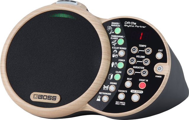 The image shows a BOSS DR-01S Rhythm Partner, a compact digital percussion instrument with a circular mesh drum pad, control panel with buttons and knobs, and a digital tempo display. It features multiple percussion sounds, tempo and volume controls, tap tempo, count-in, and a built-in speaker. Its wood-grain finish combines traditional percussion aesthetics with modern rhythm machine functionality for practice and performance.