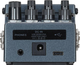 The image shows a BOSS guitar effects pedal with a blue/gray metal body, featuring eight control knobs in two rows, input/output jacks, a headphone output labeled "PHONES," a USB port, and a power input for a 9V BOSS PSA adapter. Designed as a stomp-box, it allows musicians to activate effects by foot and is used to modify and enhance the sound of electric guitars, basses, and other instruments.