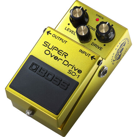 The image shows a Boss SD-1 Super OverDrive guitar pedal with a bright yellow metal housing. It features three control knobs (Level, Tone, Drive), input/output jacks on the sides, a large footswitch, and visible Boss branding. Known for adding warmth, sustain, and mild to moderate distortion, the SD-1 is a classic, versatile overdrive used in blues, rock, and more by amateur and professional guitarists.
