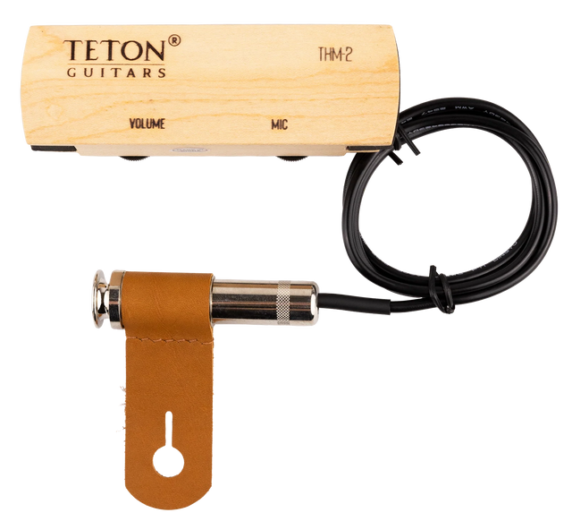 The image shows a TETON Guitars THM2 acoustic guitar pickup and preamp system. It includes a light wood preamp/control box with "VOLUME" and "MIC" controls, a black pickup cable, a chrome 1/4" output jack, and a brown leather mounting strap. Designed to amplify acoustic guitars, the hybrid system combines pickup and microphone functions, with a wooden preamp for an aesthetic fit inside the guitar.
