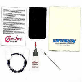 The image shows a silver wind instrument maintenance kit including a Chesbro Music Co. instruction sheet, a yellow SuperSlick polishing cloth, a black cleaning swab, a bottle of SuperSlick valve oil, a flexible cleaning brush, and black tubing or cord. This comprehensive kit provides essential tools for cleaning and caring for brass and woodwind instruments to ensure optimal performance and longevity.