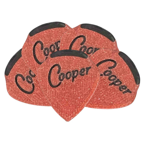 The image shows a set of teardrop-shaped Coor Cooper guitar picks with a reddish-orange sparkled finish and black decorative edges. The brand name "Coor Cooper" is printed in black on each pick. These visually striking picks are used by guitarists for plucking or strumming strings and serve as both practical playing tools and collectible items.