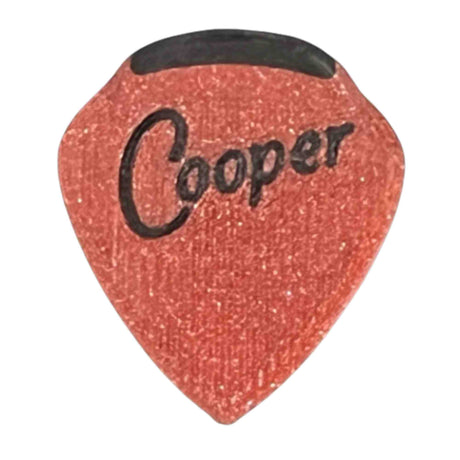The image shows a reddish-orange guitar pick with a textured, sparkly surface and black "Cooper" lettering. It features a black rubber or plastic grip at the top to prevent slipping. This common guitar accessory is used by musicians to pluck or strum strings.