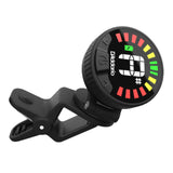 The image shows a D'Addario clip-on tuner with a circular LED display featuring red, yellow, and green segments to indicate tuning accuracy. It has a digital note readout, a black clip for attaching to instrument headstocks, and a compact design. This electronic tuner detects vibrations to help guitarists, bassists, and other string players quickly tune their instruments.