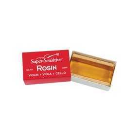 The image shows a block of "Super-Sensitive Rosin" in a light formulation, suitable for violin, viola, and cello. The translucent amber rosin is housed in red packaging labeled "Light" (No. 911). Rosin is made from tree resin and applied to bow hairs to create friction needed for sound production on string instruments. This softer rosin is preferred for warmer climates or players seeking a smoother bowing feel.