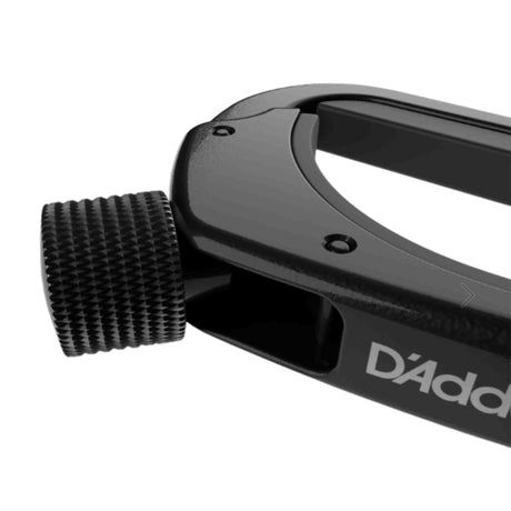 The image shows a black D'Addario guitar capo with a spring-loaded clamp and an adjustable screw with a knurled thumb wheel. Designed to clamp all strings at a fret, it raises the pitch without changing chord shapes. This professional-quality capo offers precise pressure adjustment for reliable performance, helping guitarists change keys, reach higher pitches, and create varied tonal effects.