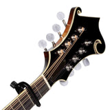 The image shows the headstock of a mandolin, a lute-family string instrument. It features a curved, ornate design with cream binding, 8 tuning pegs (4 per side) for its 4 pairs of strings, and multiple strings running down the neck. A black capo is attached. Mandolins are tuned like violins (G-D-A-E), popular in bluegrass, folk, classical, and world music for their rich, doubled-string sound.